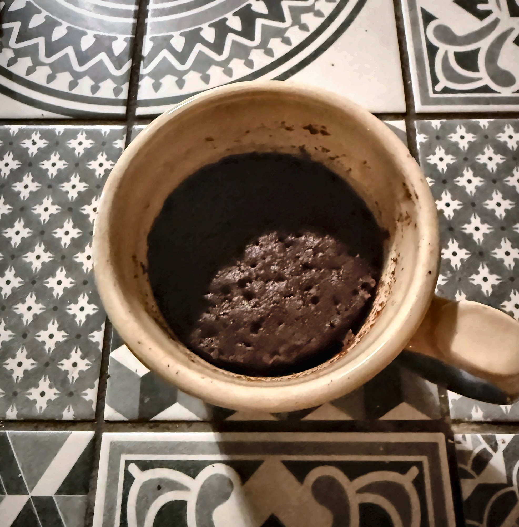 Chocolate mug cake, risen and cooked, in a cream mug on patterned tiles